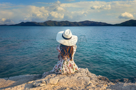 年轻女子坐在岩石顶部，看着海边。