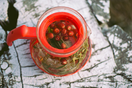 水果茶壶摄影照片_茶壶的水果茶与香草和白色树桩上的浆果。