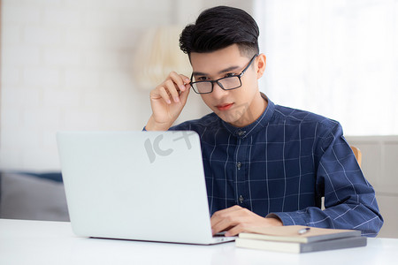 戴眼镜的年轻商人在家工作，办公桌上放着笔记本电脑，自由职业男性坐在家里，用笔记本电脑在桌上交流，创业企业家，新常态。