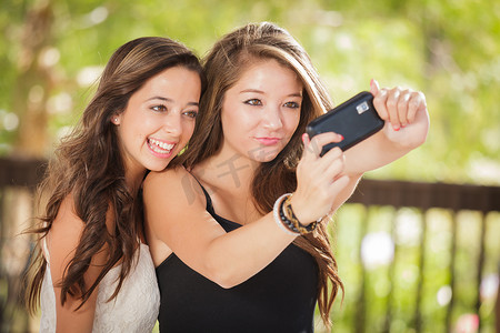 两个迷人的混血女友在户外使用智能手机自拍