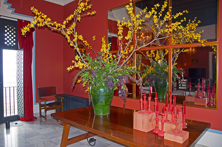 墙上的蜡烛摄影照片_桌上有黄色花朵和红色蜡烛的大绿色花瓶，墙上有镜子，红色内饰