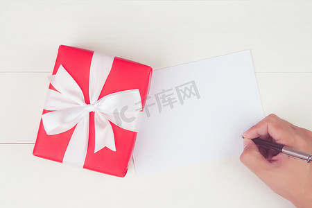 男人用空白贺卡写信，木桌上有红色礼品盒，礼物和包装，明信片模型，顶视图，平躺，复制空间，假日概念。
