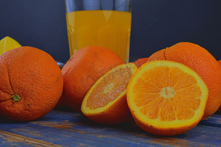 挤压机摄影照片_橘子、橙子、一杯橙汁和蓝色木质背景上的手动柑橘榨汁机。