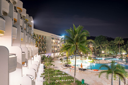 夜间酒店度假村阳台的侧景，游泳池和明亮的灯光反射在蓝色游泳池水中长时间曝光