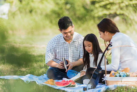 鲜花的男人摄影照片_亚洲家庭在公园里享受户外野餐毯阅读书的乐趣
