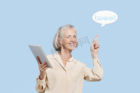 高级英语摄影照片_蓝色背景下手持平板电脑的高级女性肖像指着推文气泡