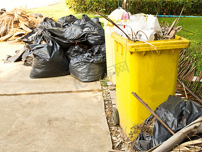 路边垃圾桶摄影照片_花园里黄色垃圾桶里的垃圾。