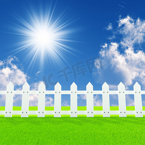 绿色栅栏摄影照片_阳光明媚的夏日草坪上的白色栅栏