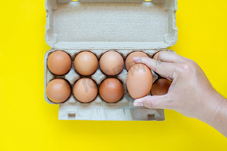 男人的手在纸箱里捡起一个棕色的鸡蛋。