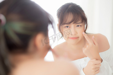 肖像美丽的亚洲年轻女性照镜子是痤疮、青春痘治疗、女孩问题美容脸，完美地与家里卧室的健康相结合，具有皮肤护理和保健概念。