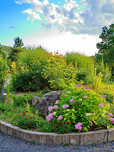 绿化路摄影照片_一个五颜六色的花坛，上面有鲜艳的花朵和绿草，里面有大石头，周围环绕着路缘石。