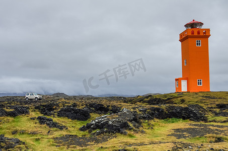 冰岛岩石上橙色灯塔前的汽车，