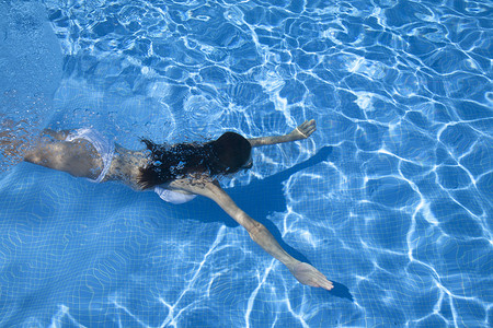 张开双臂的女人在游泳池里潜水