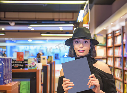 书店的人摄影照片_美丽的女人拿着并展示一本书。