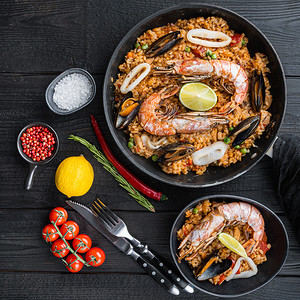 传统平底锅中典型的西班牙海鲜海鲜饭和黑色木质背景中的黑色碗，平铺