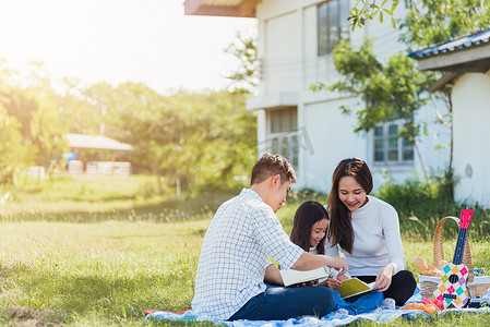 亚洲家庭在公园里享受户外野餐毯阅读书的乐趣