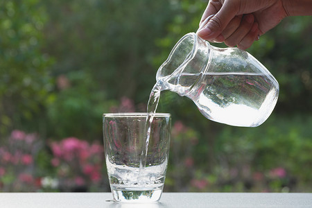 自然背景摄影照片_自然背景下，女手从罐子里往玻璃杯里倒水