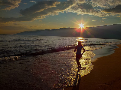 孩子奔跑剪影摄影照片_夕阳下的剪影年轻女孩在海边奔跑