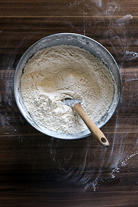 在深色木制背景上用抹刀在碗里撒面粉。