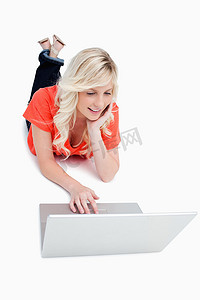 年轻的金发女人躺在地板上使用笔记本电脑