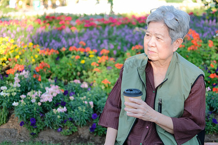 亚洲老年老年妇女在花园里喝咖啡茶。