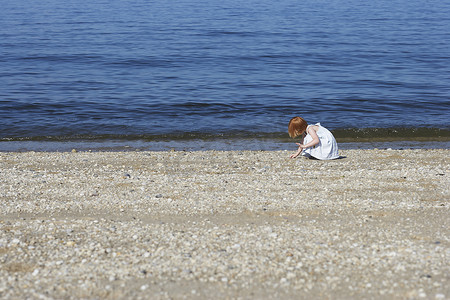 小女孩在沙滩上捡贝壳的侧视图