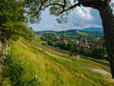 铁轨风景摄影照片_倾斜的绿色斜坡，底部环绕着村庄，延伸到远处的铁轨