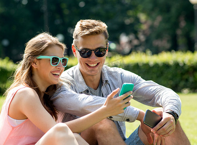 带着智能手机坐在公园里微笑的朋友