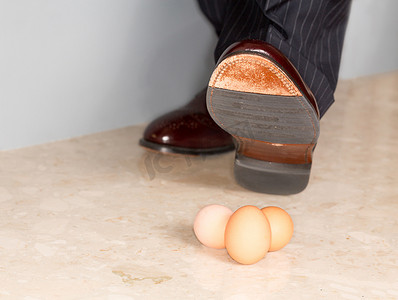 小心压脚摄影照片_男人的鞋子踩在三个鸡蛋上