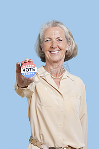 高级英语摄影照片_蓝色背景下手持选举徽章的高级女性肖像
