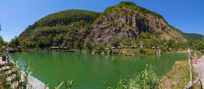 在炎热的夏日，池塘的美丽景色位于两座山脚下，山坡上有石质山坡，森林杂草丛生。