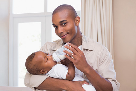 可爱的奶瓶摄影照片_快乐的父亲给他的男婴喂奶瓶