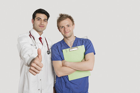 一位印度医生在浅灰色背景下与男护士站在一起时竖起大拇指的肖像