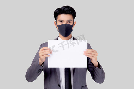 戴着面罩的年轻亚洲商人画像展示了白色背景中孤立的纸片、因 covid-19 危机而失业的商人、covid 的经济和流行病、检疫和口号。