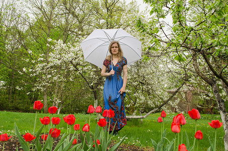 穿着裙子的女孩拿着雨伞摆着公园花