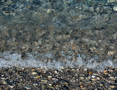 小波浪在被鹅卵石和鹅卵石覆盖的海边破碎