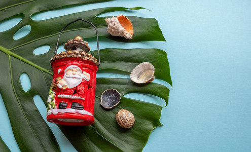 蓝色背景、贝壳、圣诞手电筒上的热带绿叶龟背竹。