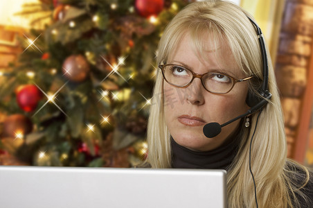 圣诞树和电脑前戴着耳机的心烦意乱的女人