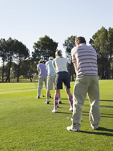 在高尔夫球场上排成一排的年轻高尔夫球手的后视图