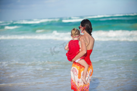 母女俩穿着红裙走在沙滩上的背影