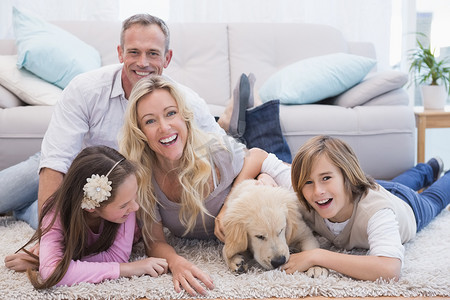 黄色房屋摄影照片_笑着的一家人在地毯上放着他们的宠物黄色拉布拉多犬