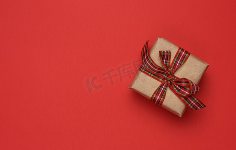 盒子正方形摄影照片_方形盒子，里面有用牛皮纸包裹的礼物，并用红色丝带系着
