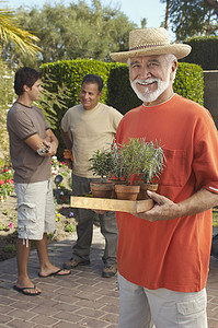 一个快乐的老人拿着盆栽的肖像，男人站在背景中