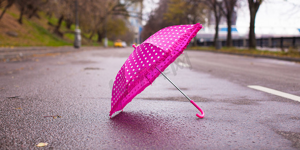 户外湿沥青上的粉红色儿童伞