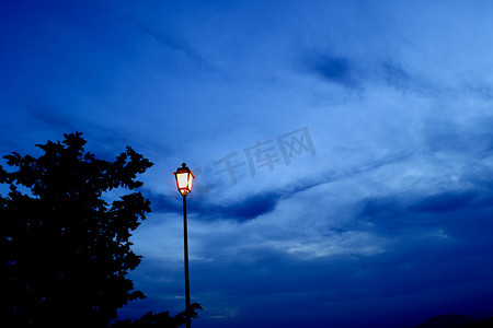 烟花点亮夜空摄影照片_蓝色时刻点亮的旧灯、树剪影和蓝天