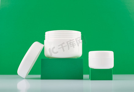 护肤品绿色背景摄影照片_关闭讲台上两个白色光滑的奶油罐反对绿色背景与文本的空间。