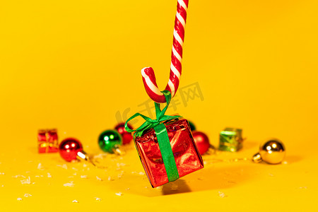 新年糖果摄影照片_糖果手杖棒棒糖拿着一个礼盒，里面有黄色背景的圣诞礼物，圣诞糖果和新年装饰