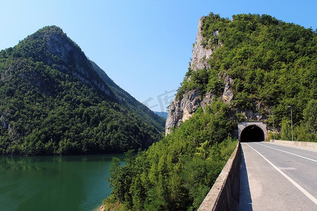 黑峡谷摄影照片_德里纳河峡谷（波斯尼亚和黑塞哥维那）上的公路和隧道在夏季被树木覆盖的山脉所环绕