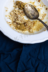 选择样式摄影照片_深蓝色背景的白色盘子里剩下的辣鸡肉咖喱和米饭。