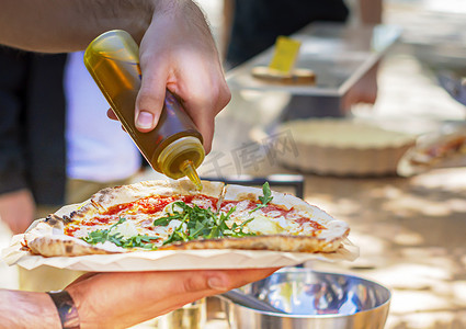 倒油瓶摄影照片_一名男性正在倒橄榄油给比萨调味。